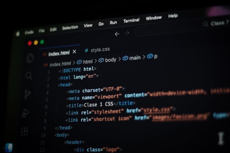 A close-up view of a person's hands typing on a laptop keyboard positioned on a dark surface, with the screen displaying a code editor or programming interface featuring multiple lines of colored text